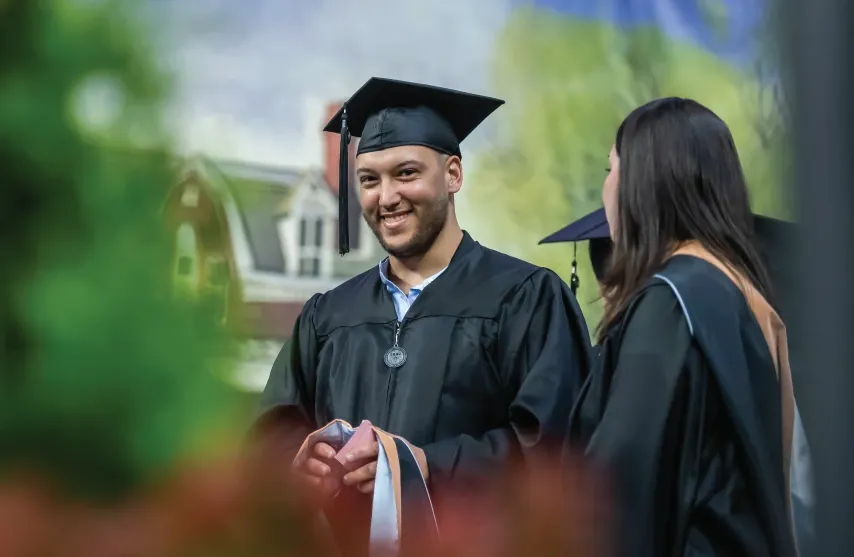 Graduate on stage smiling in cap and gown.